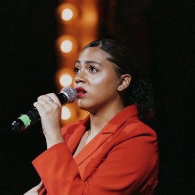 Amyah-Recital-red-square-512 Amyah in a red jacket holding a microphone and singing.